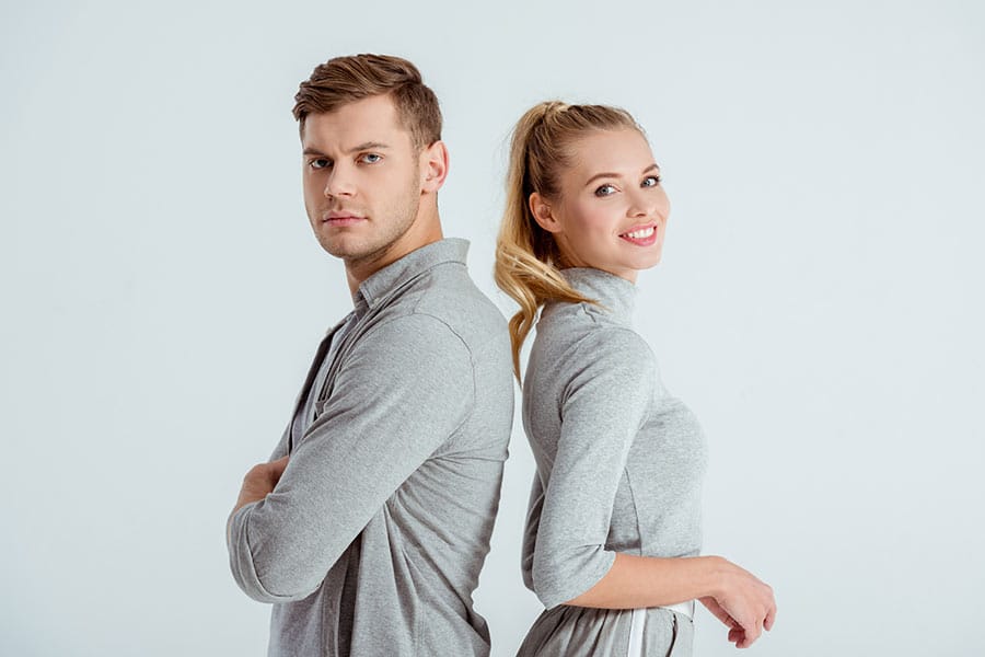 Couple standing back-to-back, man serious, woman smiling.